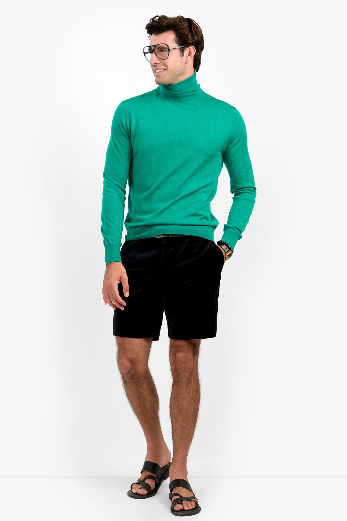 A man wearing glasses, the WOODROW TURTLENECK, black shorts, a watch, and black sandals stands against a white background, smiling and looking to his left.