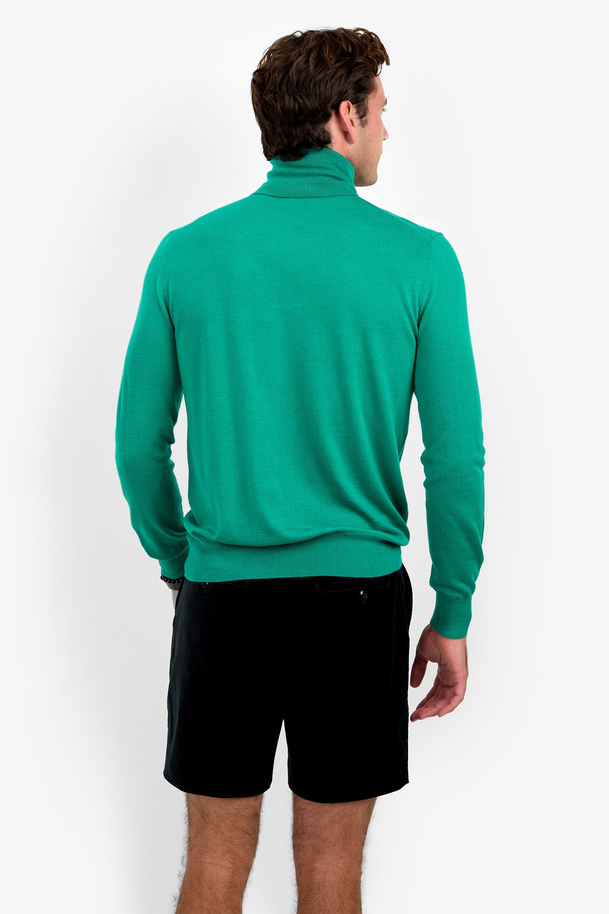 A man stands facing away, wearing the WOODROW TURTLENECK in green and black shorts against a plain white background.