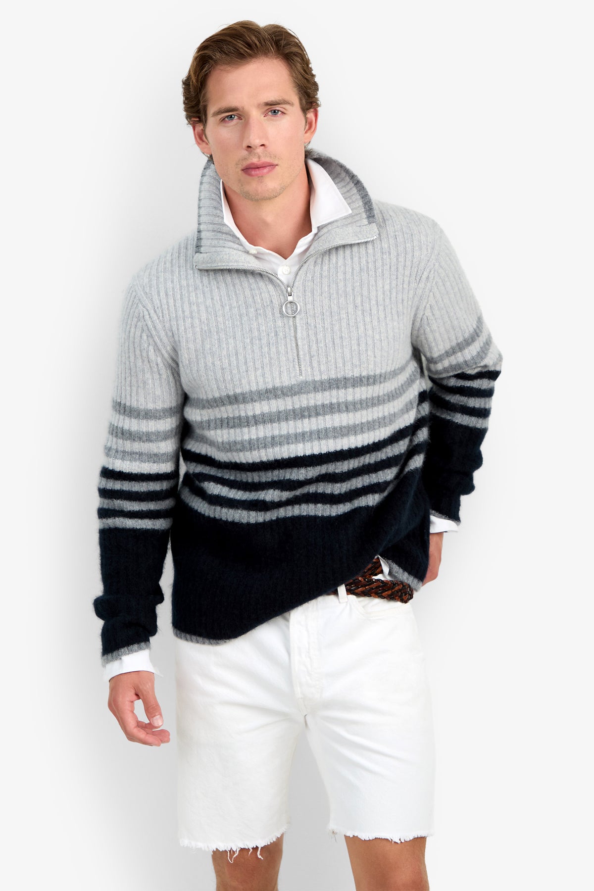 A man wearing the HEMMINGWAY QUARTER ZIP PULLOVER—a gray and black striped sweater with a zipper collar—and white shorts stands against a plain white background, looking at the camera.