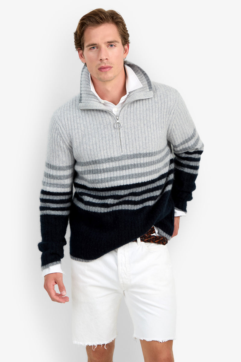 A man wearing the HEMMINGWAY QUARTER ZIP PULLOVER—a gray and black striped sweater with a zipper collar—and white shorts stands against a plain white background, looking at the camera.