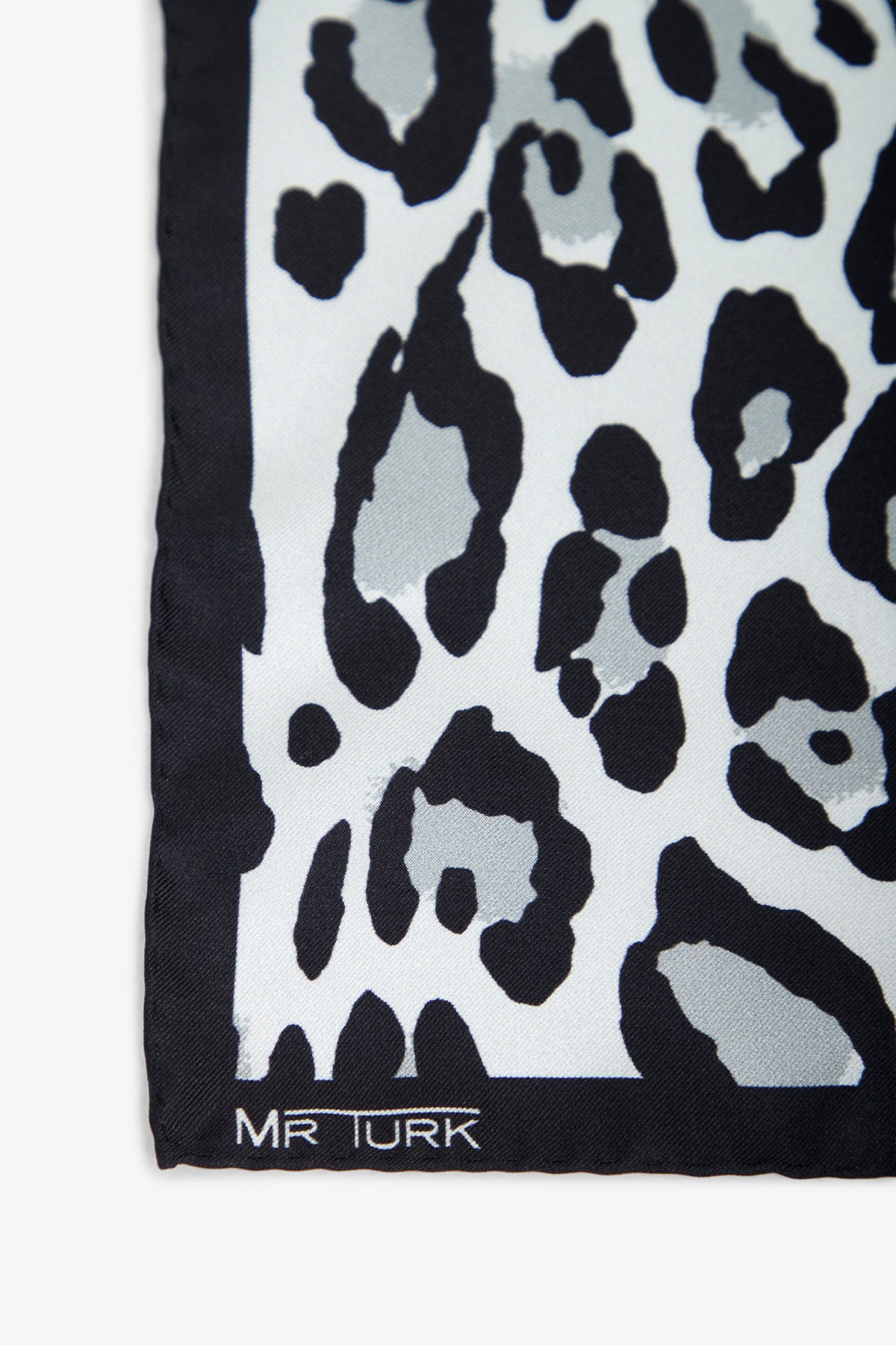 Close-up of a fabric corner with a black and gray leopard print pattern. The text Snow Leopard Pocket Square is printed in white on the black border at the bottom left.