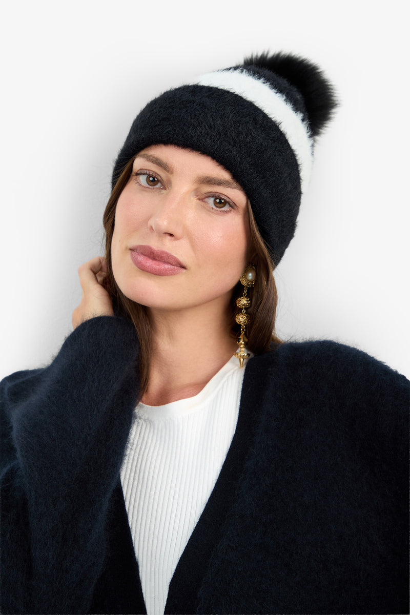 A person wears a RAJA HAT, a black nylon beanie featuring a white stripe and a black pom-pom.