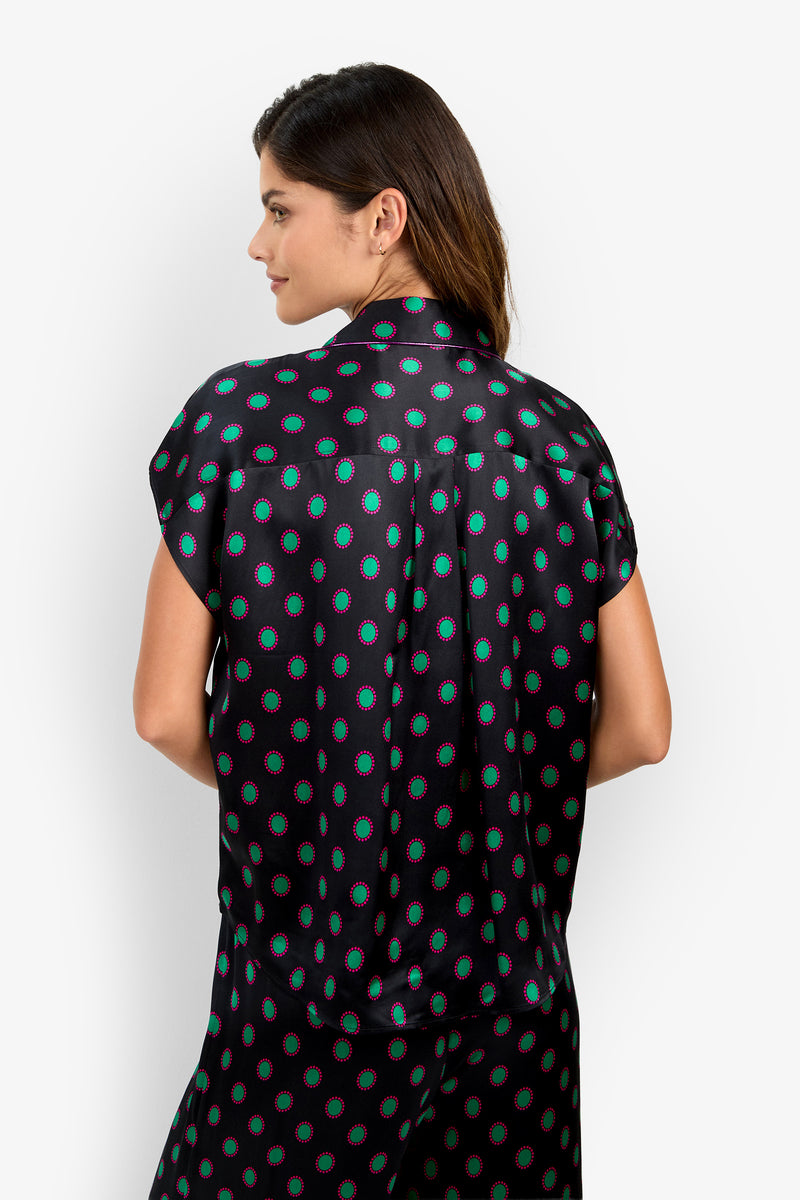 The ADARA 2 TOP is a short-sleeved, collared button-up made of silk, featuring a black background with a green and pink circular pattern.