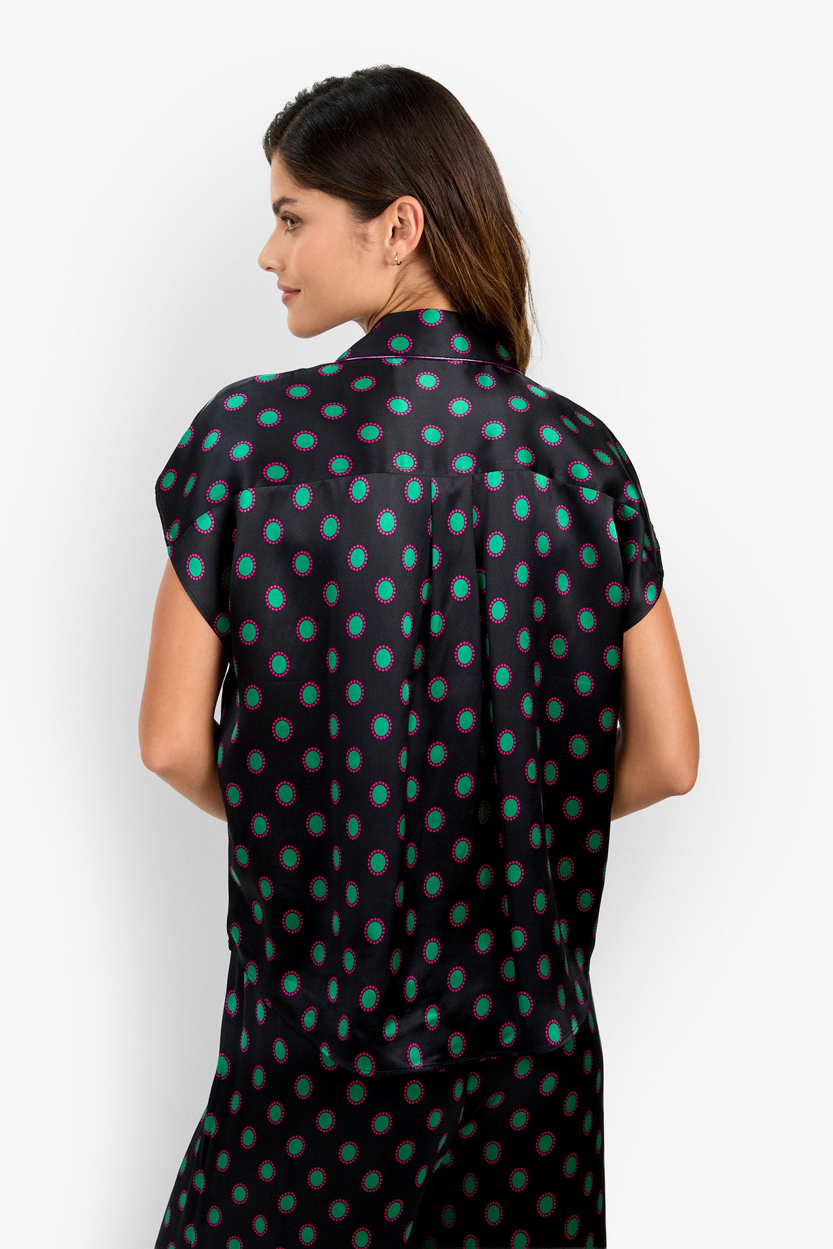 The ADARA 2 TOP is a short-sleeved, collared button-up made of silk, featuring a black background with a green and pink circular pattern.