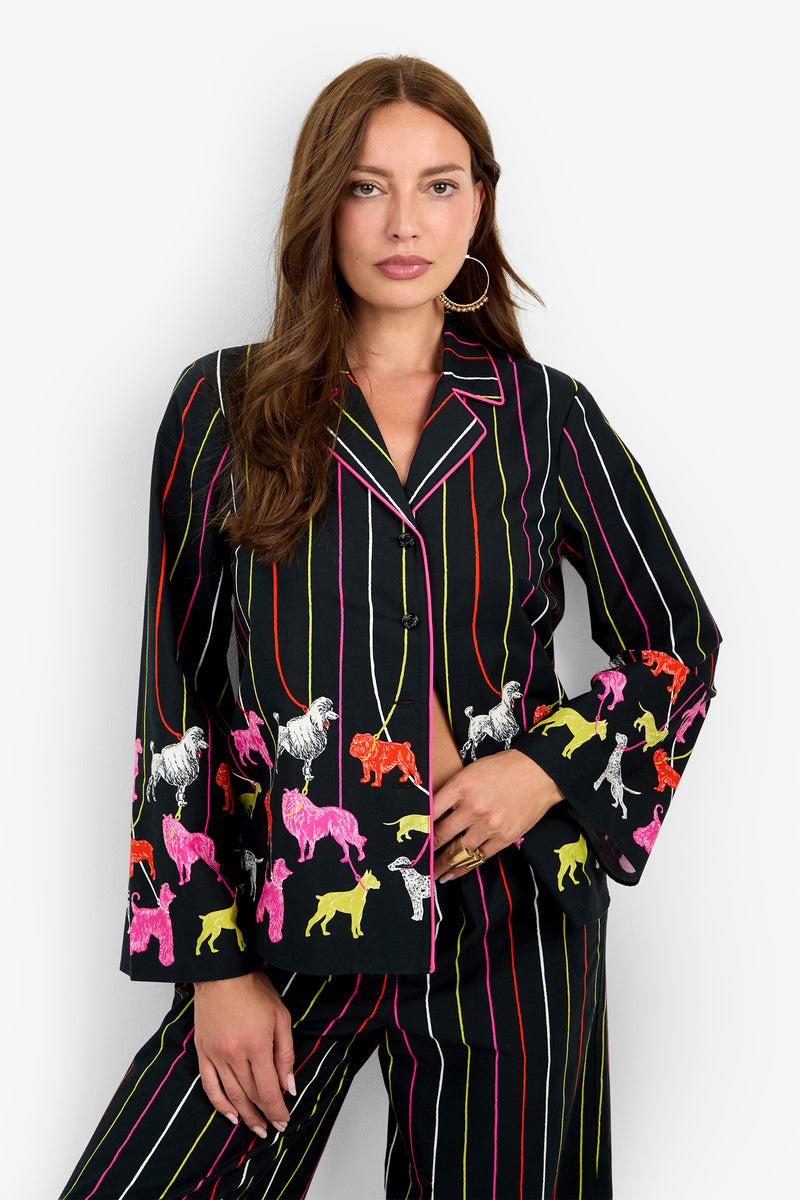 The ANNAH TOP is a black 100% cotton button-down shirt featuring vertical stripes and a colorful dog pattern along the cuffs and hem.