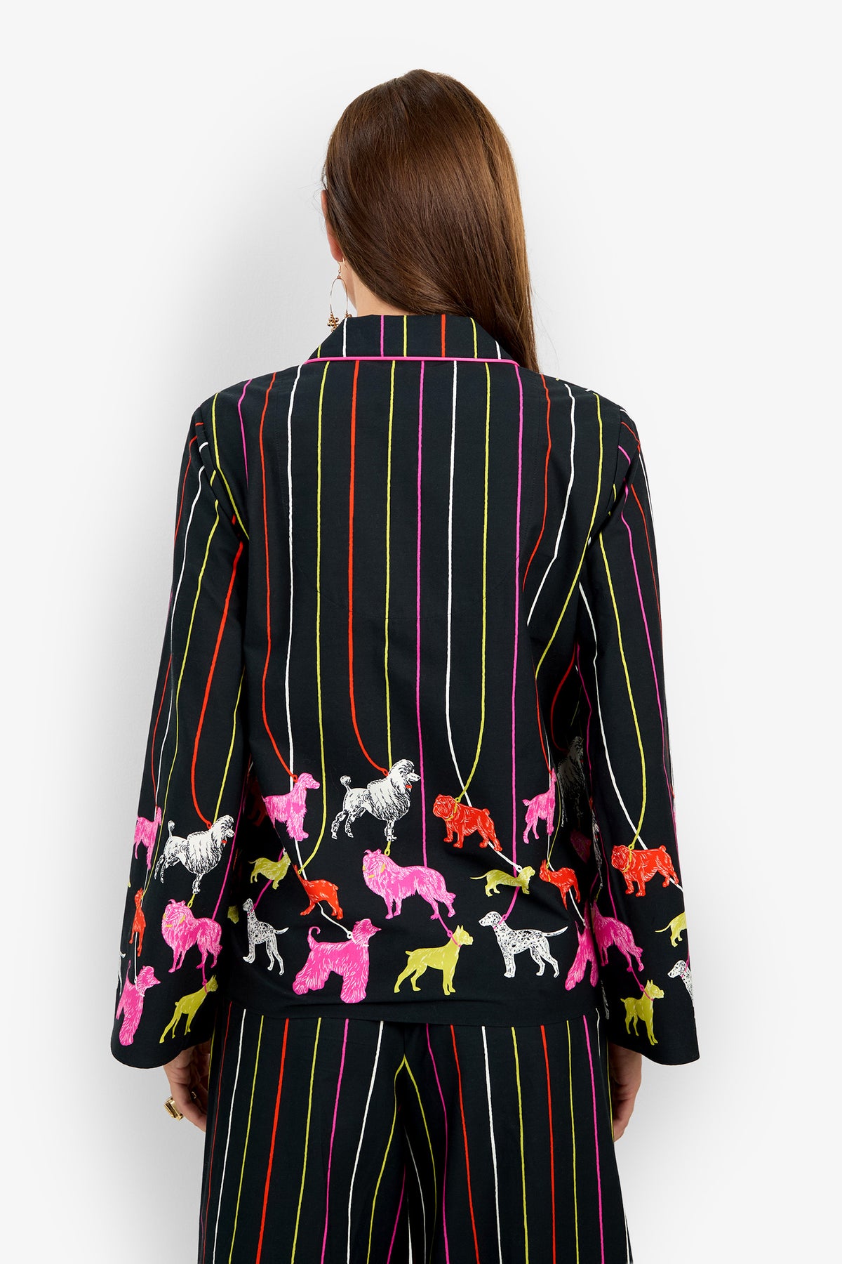 Back view of a person wearing the black ANNAH TOP, a 100% cotton blazer featuring vertical multicolored stripes and a pattern of colorful dogs on leashes along the hem.
