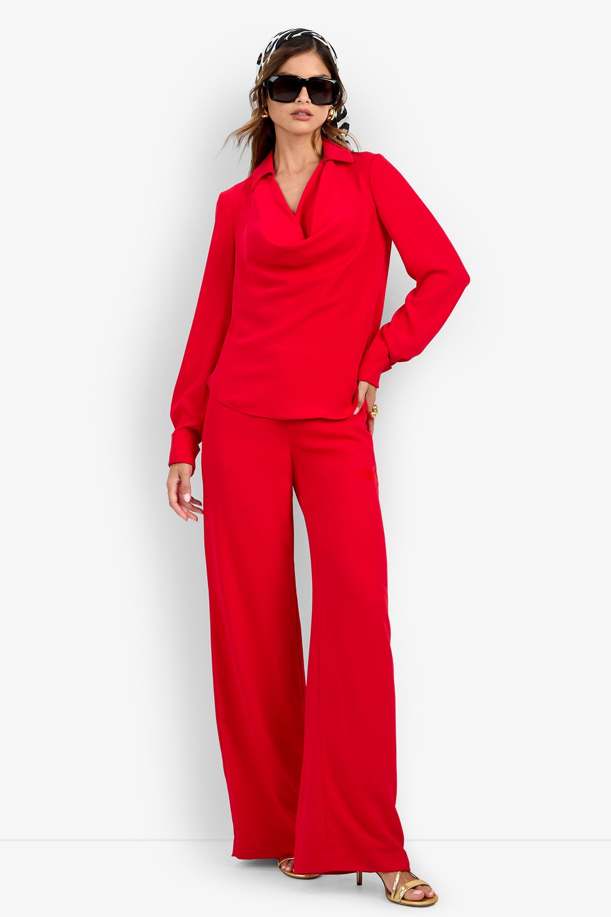 A person wearing a red MISTIC TOP with a cowl neck and matching polyester wide-leg trousers, styled with oversized sunglasses and a patterned headscarf.