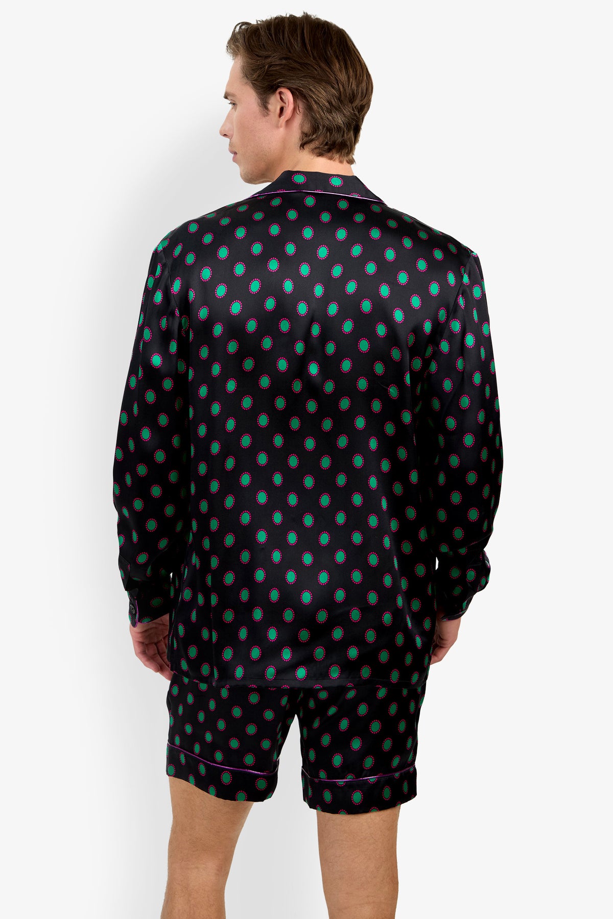 A man seen from behind wearing a PJ TOP made of 100% silk long-sleeved top and matching shorts, featuring a pattern of green and pink oval dots with purple trim.