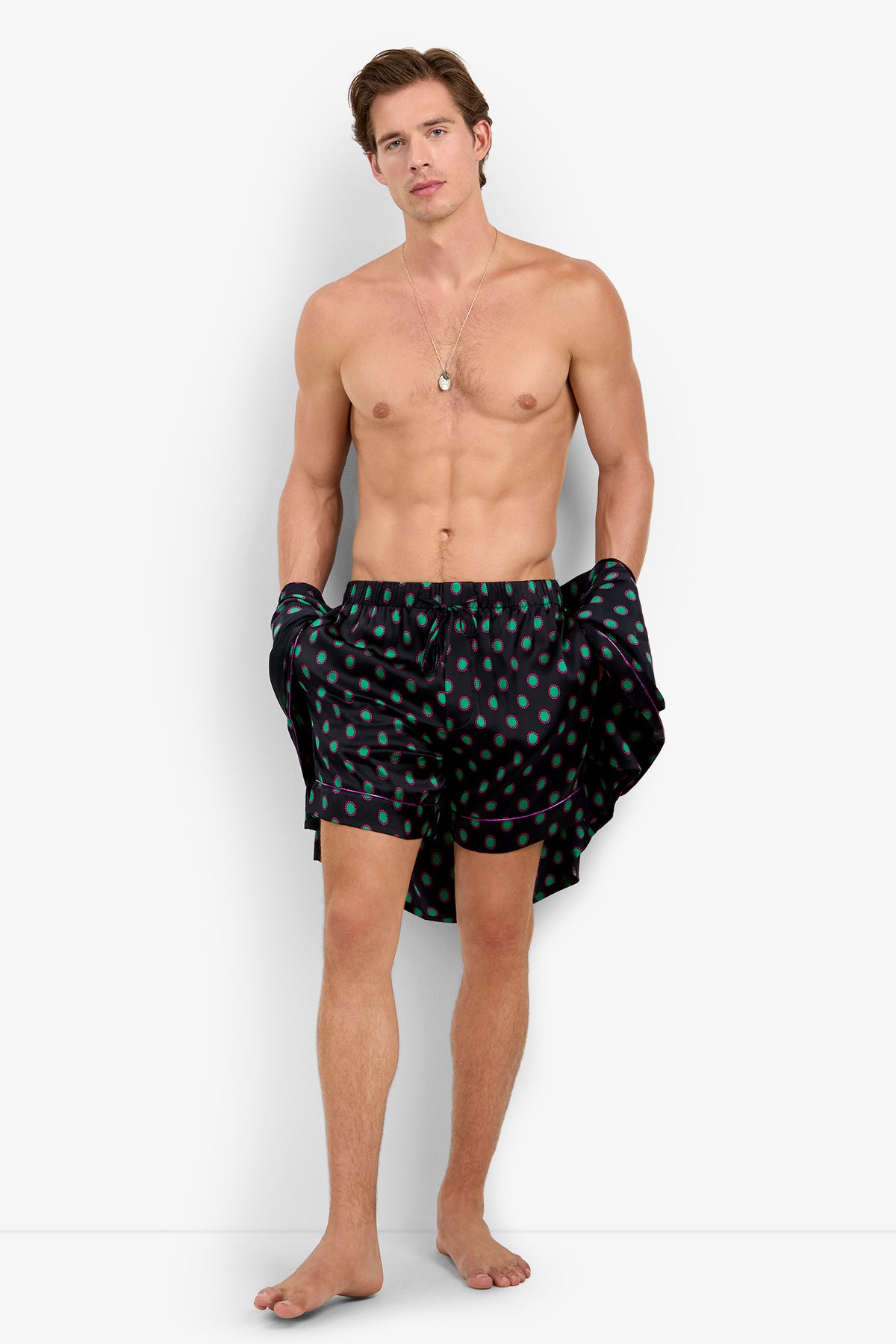 A man wearing PJ SHORT in pure silk with a teal polka dot pattern and purple piping.