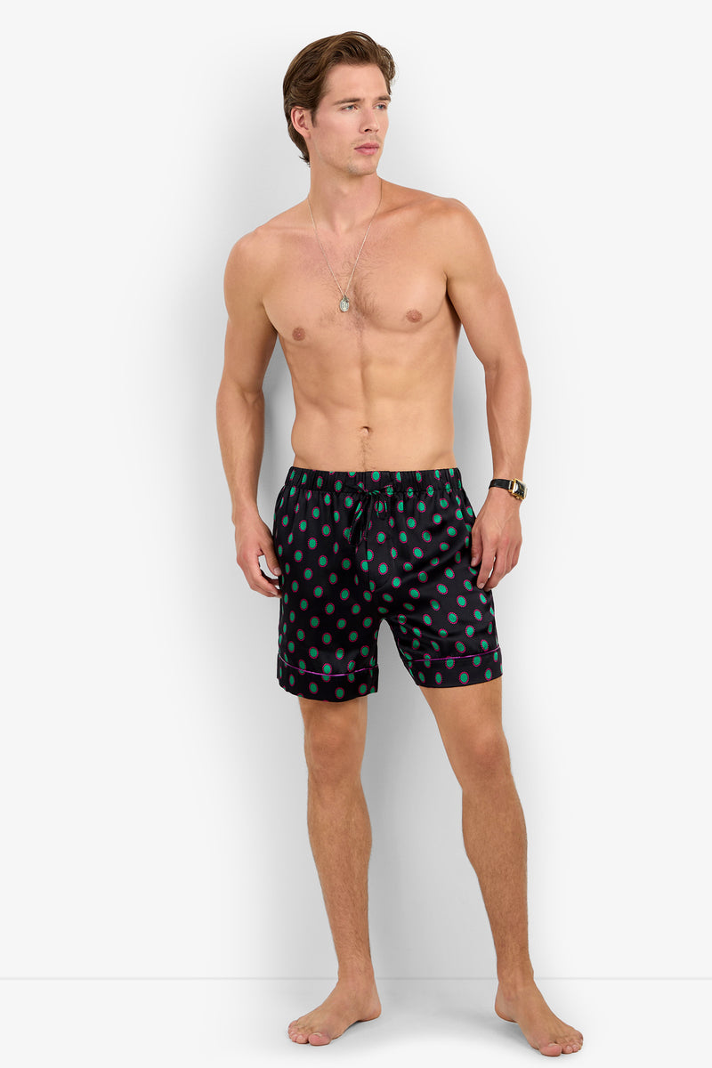 A shirtless man wears Silk PJ Short black pajama shorts with a green polka dot pattern and pink piping.