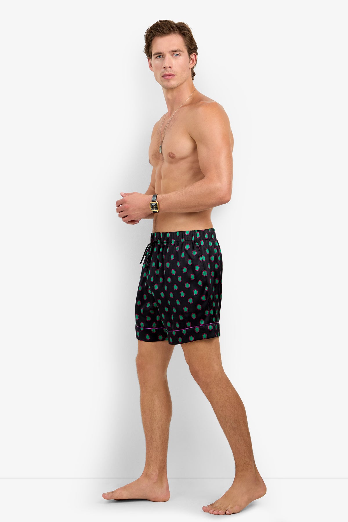A man wearing PJ SHORT 100% silk pajama shorts in black with a green polka dot pattern and pink trim.