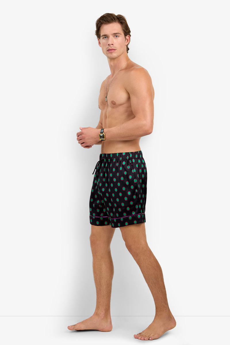 A man wearing PJ SHORT 100% silk pajama shorts in black with a green polka dot pattern and pink trim.