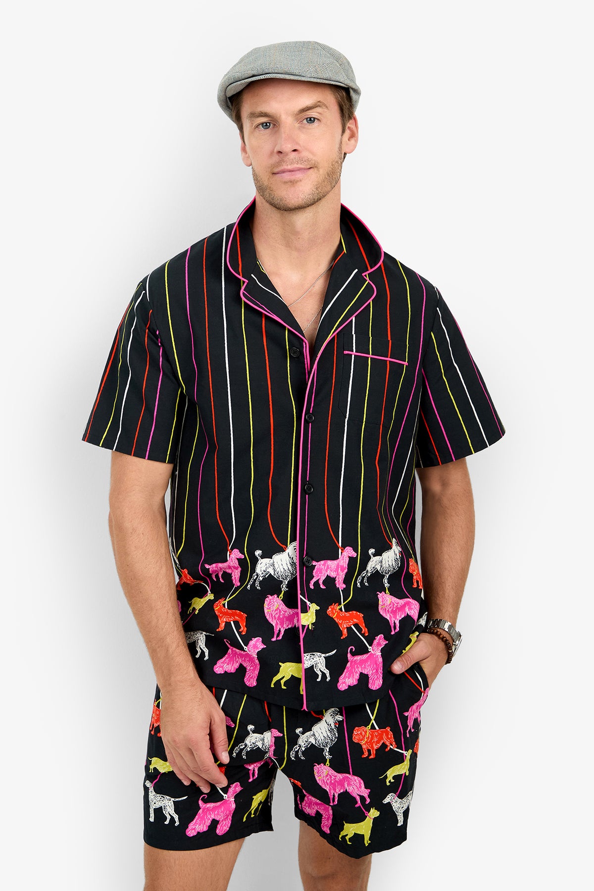 A man wears a black PJ SHORT set featuring short sleeves, matching shorts, vertical stripes, and a colorful pattern of small dogs.