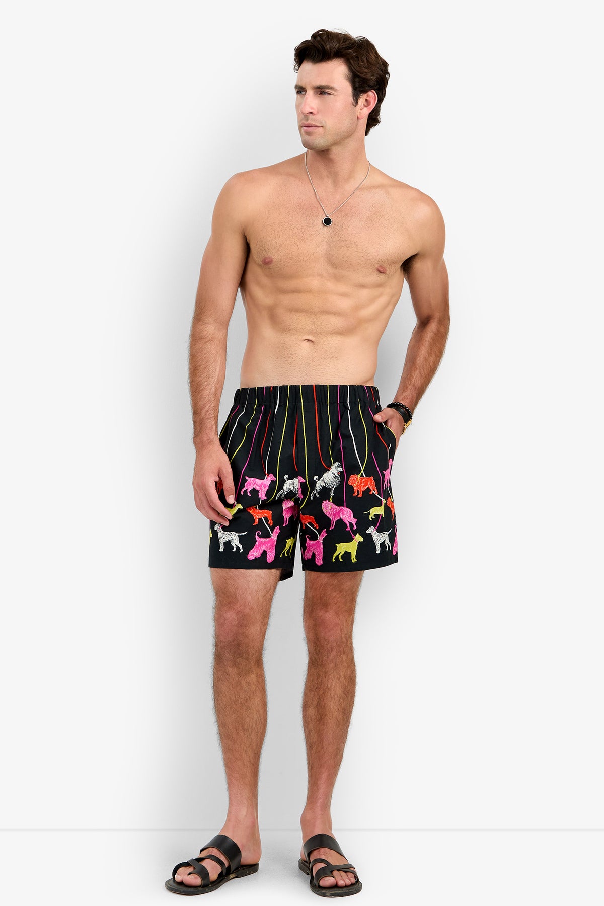 A man wears black PJ SHORT featuring a colorful pattern of dogs on leashes.