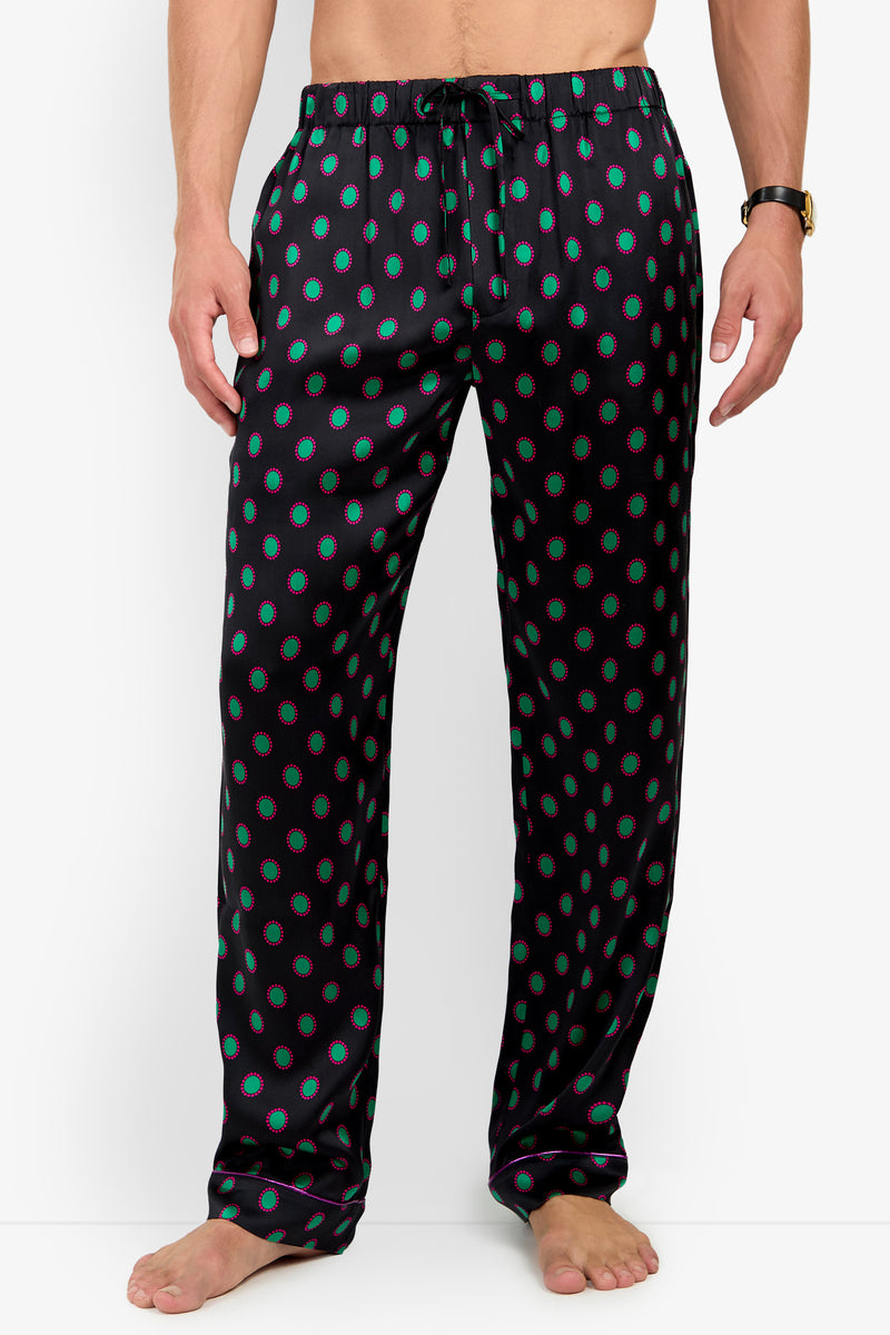 A person wearing PJ PANT silk pajama pants with a repeating pattern of green ovals outlined in pink and a drawstring waistband.