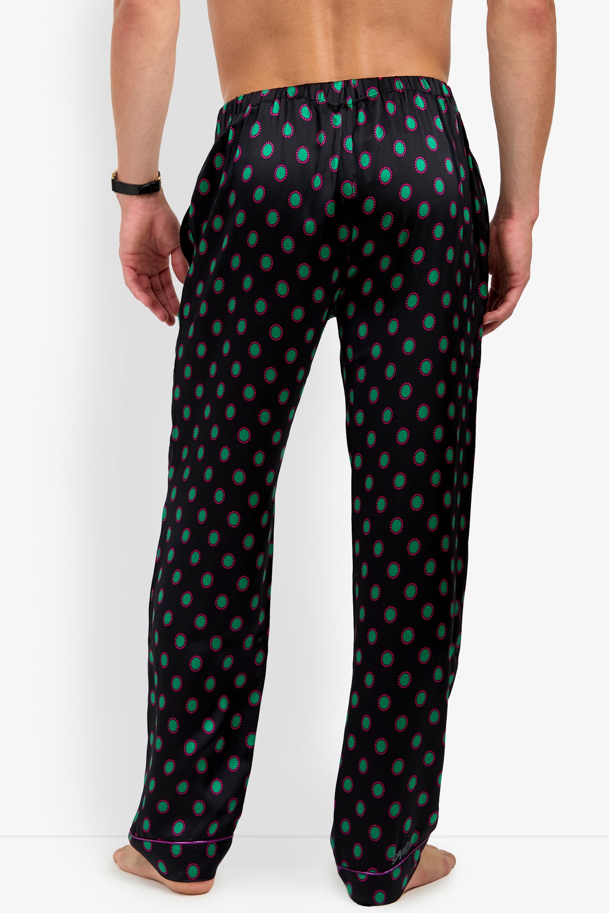 Back view of a person wearing black PJ PANT 100% silk pajama pants featuring a repeating pattern of green circles outlined in pink.