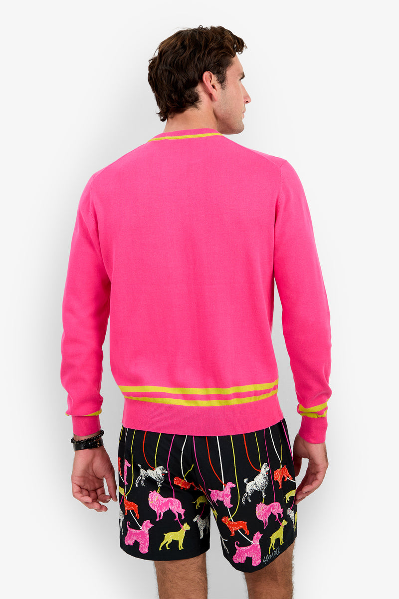 A person seen from behind wearing the bright pink PALM SPRINGS CREWNECK with yellow striped cuffs and hem, paired with black shorts featuring a colorful poodle print.