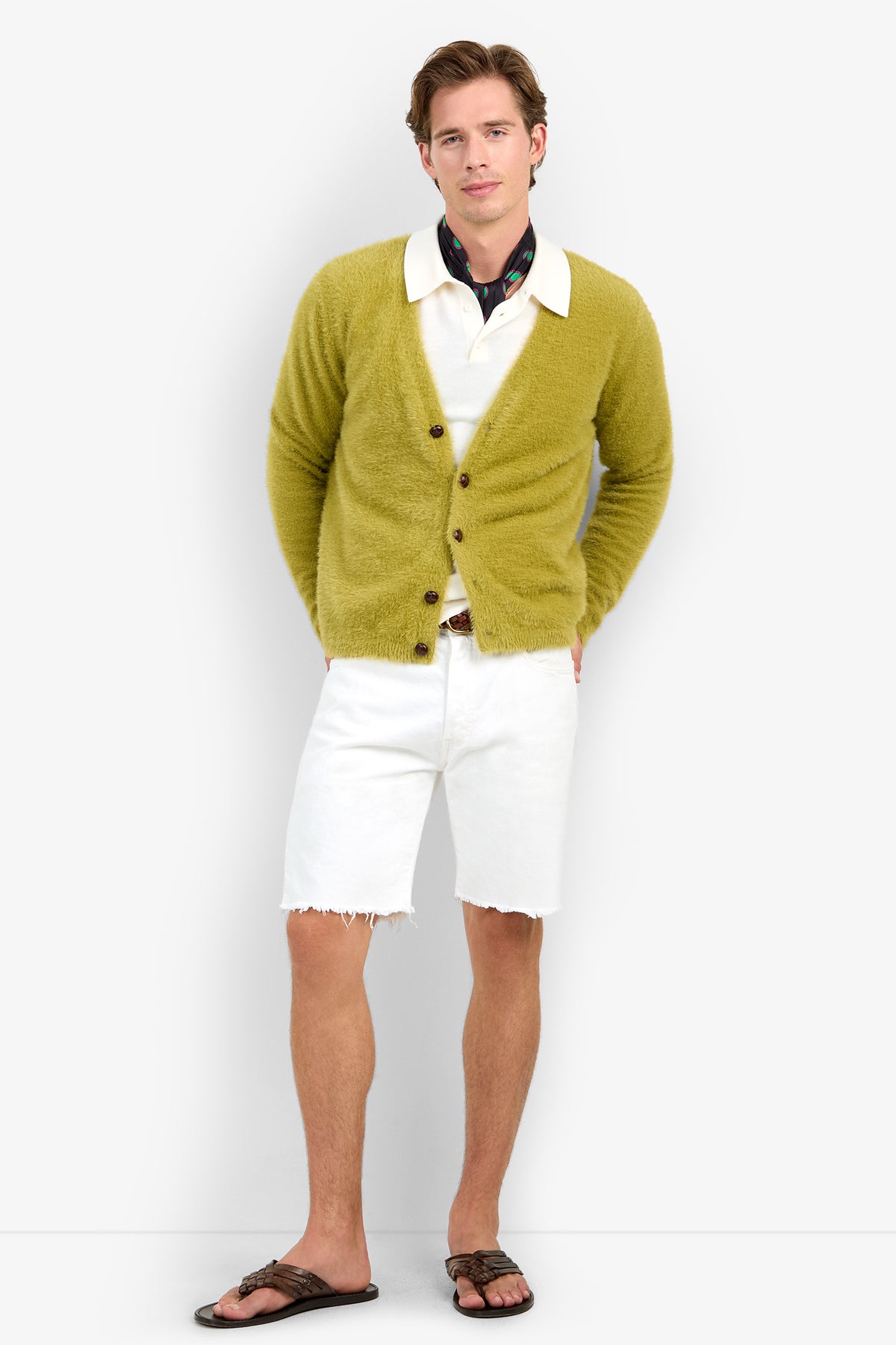 A man wears a fuzzy, chartreuse V-neck SCOTT FUZZY CARDIGAN made of 100% polyester over a white polo shirt and white denim shorts with a raw hem.