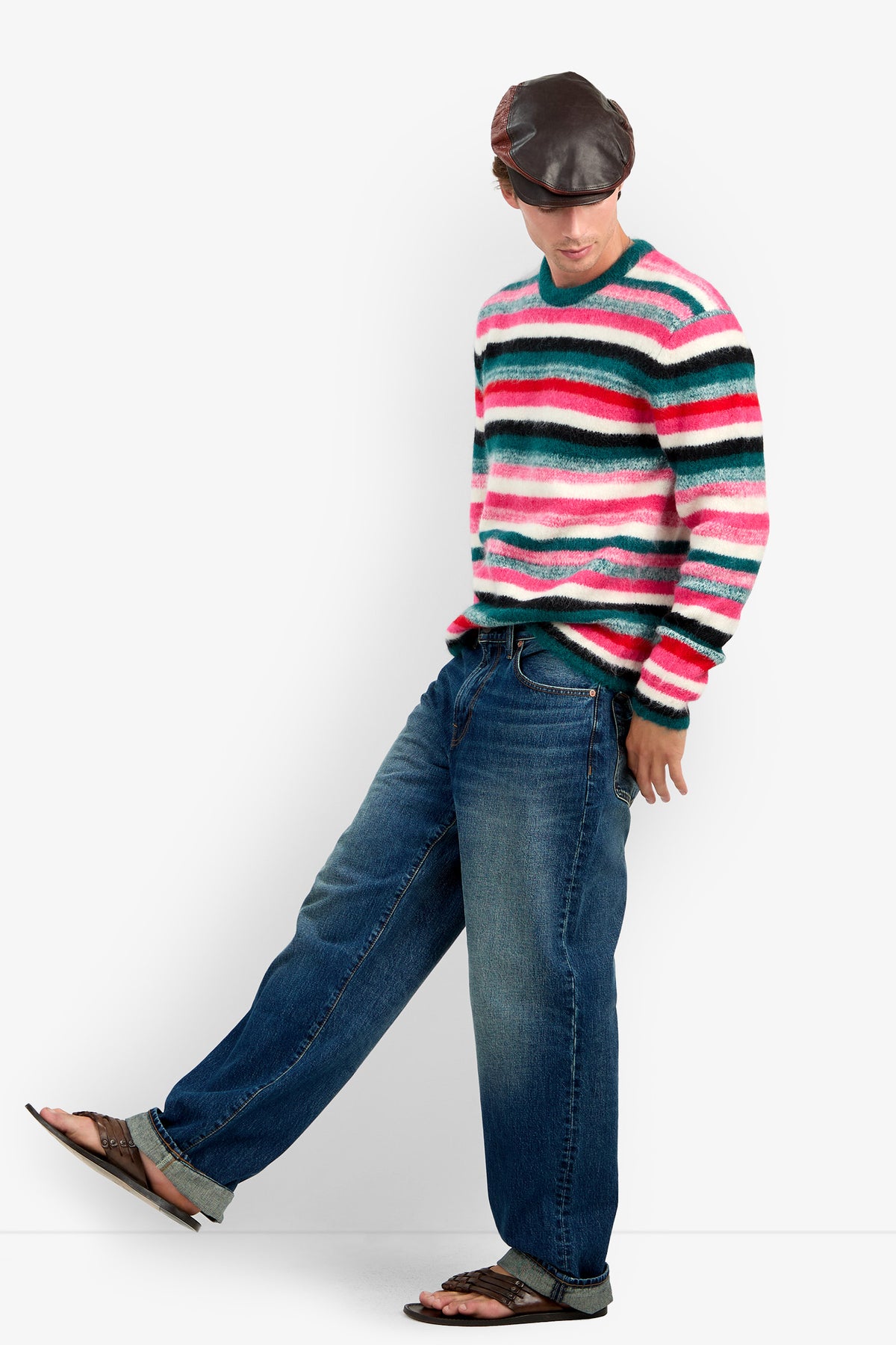A person wearing a MR. BARDINI striped cashmere crew-neck sweater, blue jeans, a leather cap, and sandals.