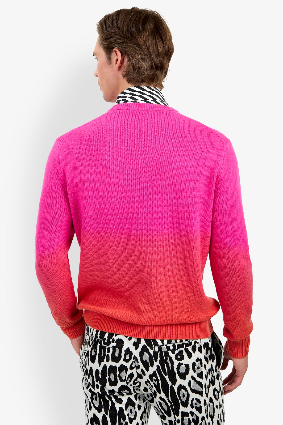 A person viewed from behind wears a pink-to-red ombre TIMOTHY OMBRE cashmere sweater over a black-and-white patterned shirt and leopard-print pants.