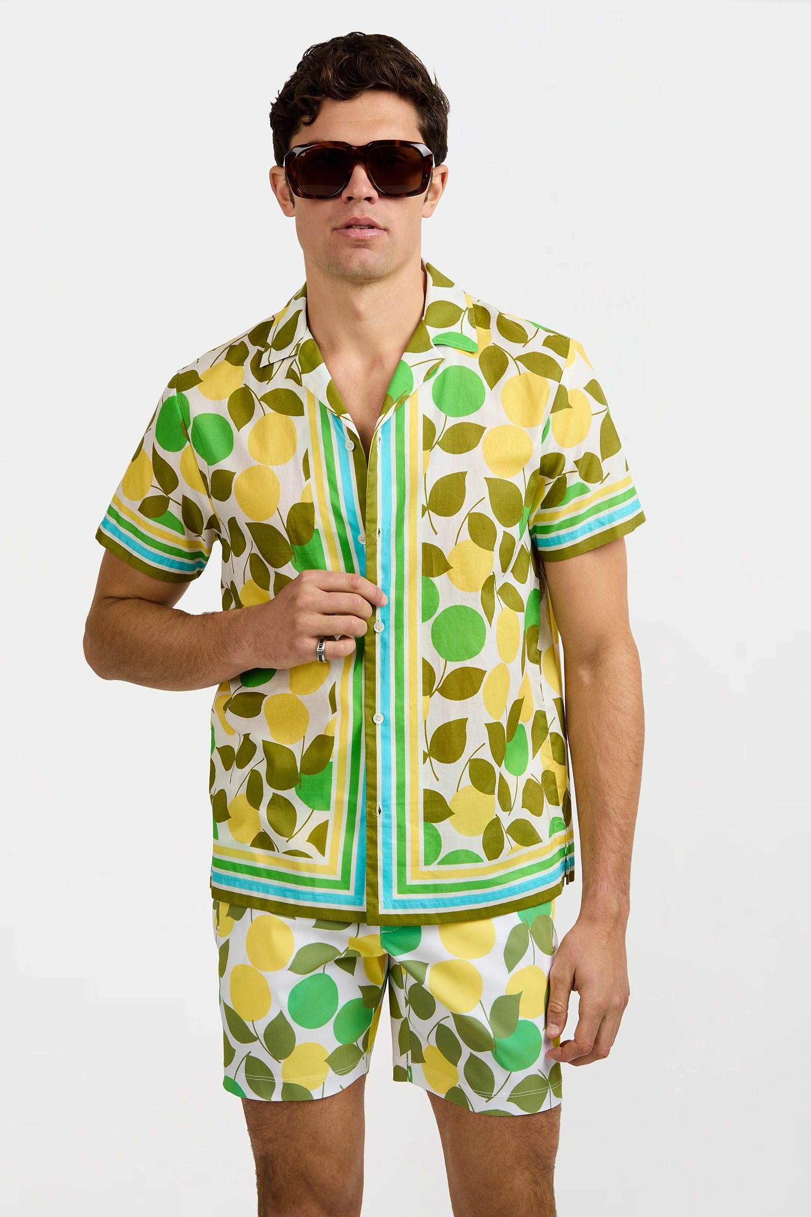 A man wearing the Josue Short-Sleeve Shirt - Limone, featuring a bold yellow lemon and green leaf print, paired with matching shorts, stands against a plain white background.