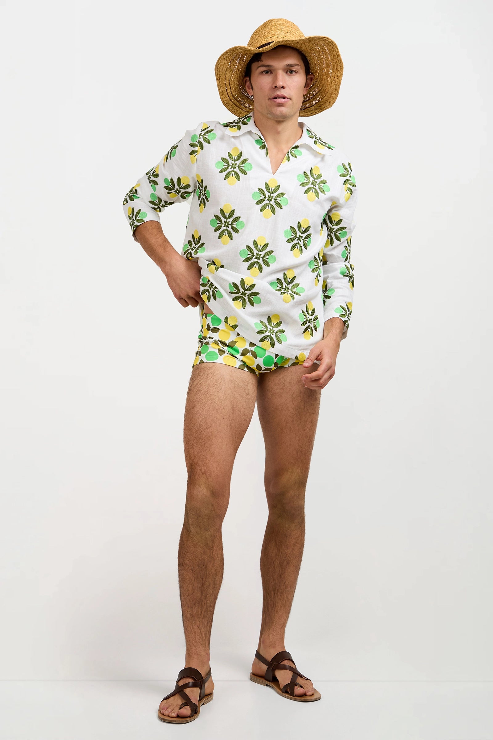 A person wearing the Holmes Pullover, paired with patterned swim trunks, a straw hat, and brown sandals stands against a plain white background.