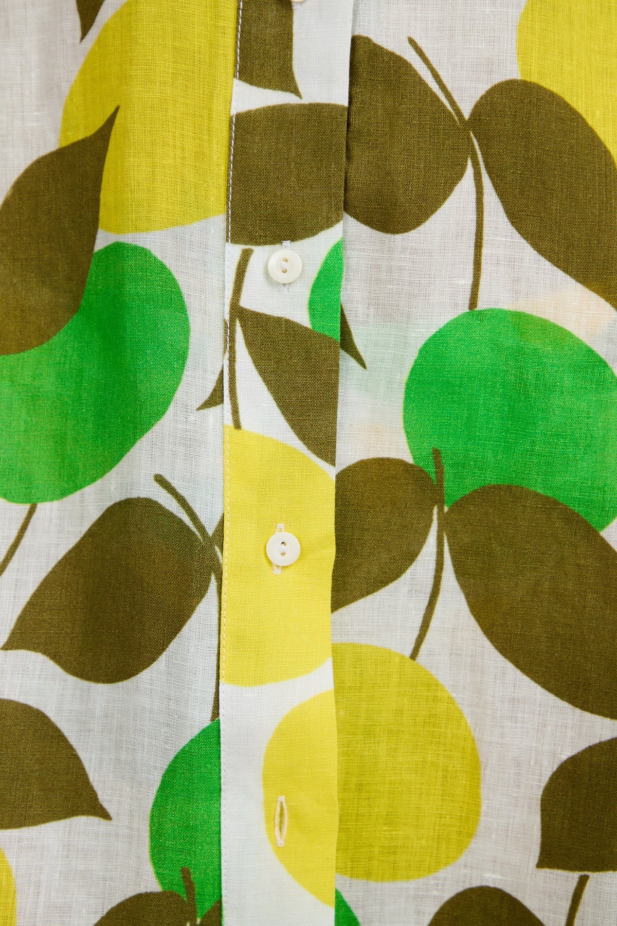 Close-up of the Opponent Shirt Dress fabric with a colorful leaf pattern in green, yellow, and brown on white, featuring a button-up design and two visible white buttons.