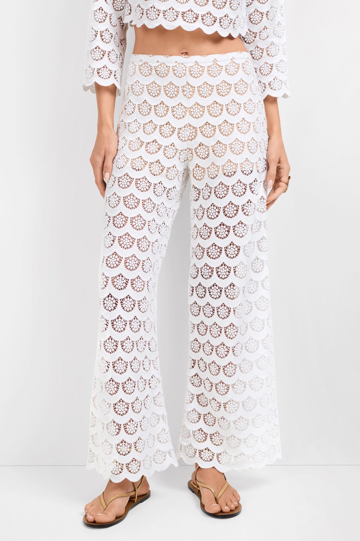 A person is wearing Dzo Dzo Crochet Lace Pants with a matching white cropped top. The high-waisted outfit features an intricate lace openwork pattern and is styled with tan sandals.