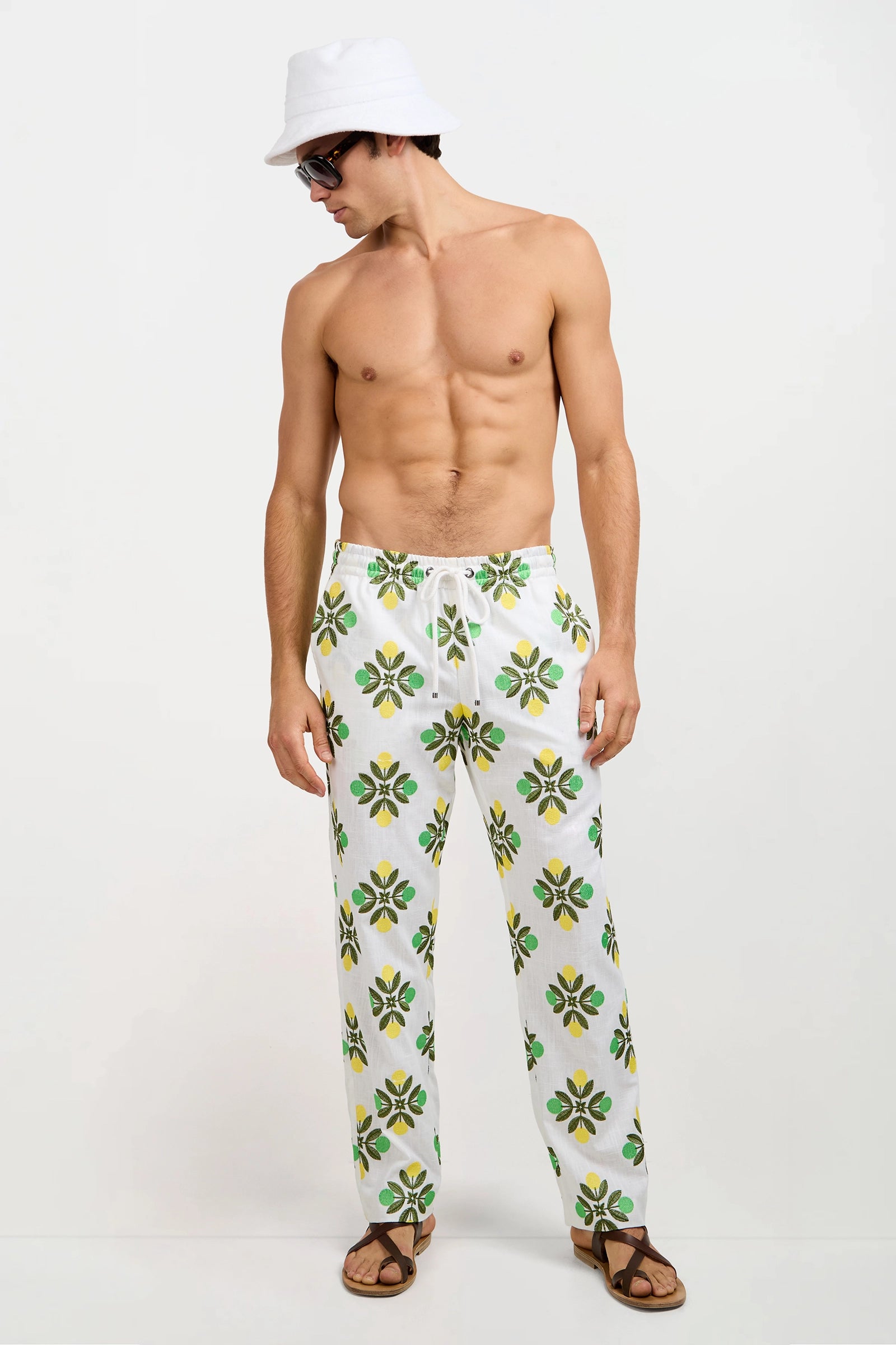 A shirtless man wearing patterned white pants, brown sandals, sunglasses, and the Gilligan Bucket Hat - Linsk Terry stands against a plain white background.