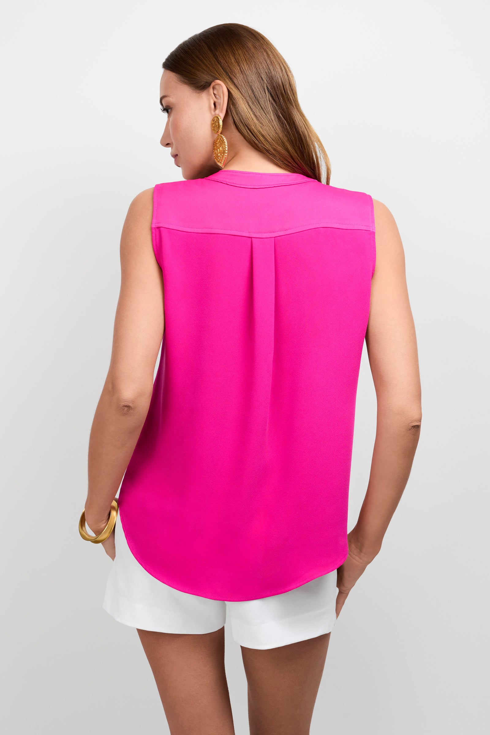 Woman shown from the back wearing the bright pink Sleeveless Kaiko Top and white shorts, accessorized with gold earrings and a gold bracelet, standing against a plain light background.