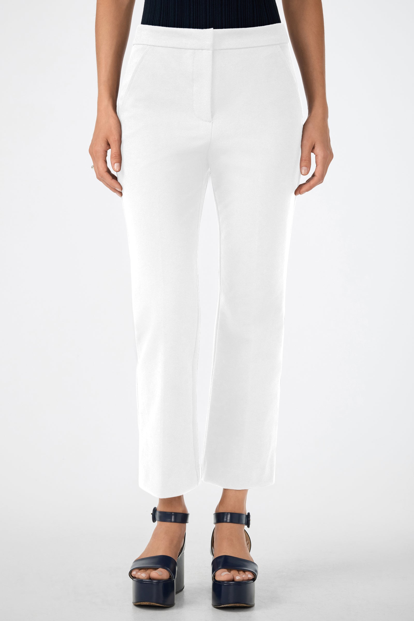A woman’s lower body is shown against a plain background, wearing Banshee Cropped Cuff Hem Pants in white and navy blue platform sandals, with her hands resting by her sides.