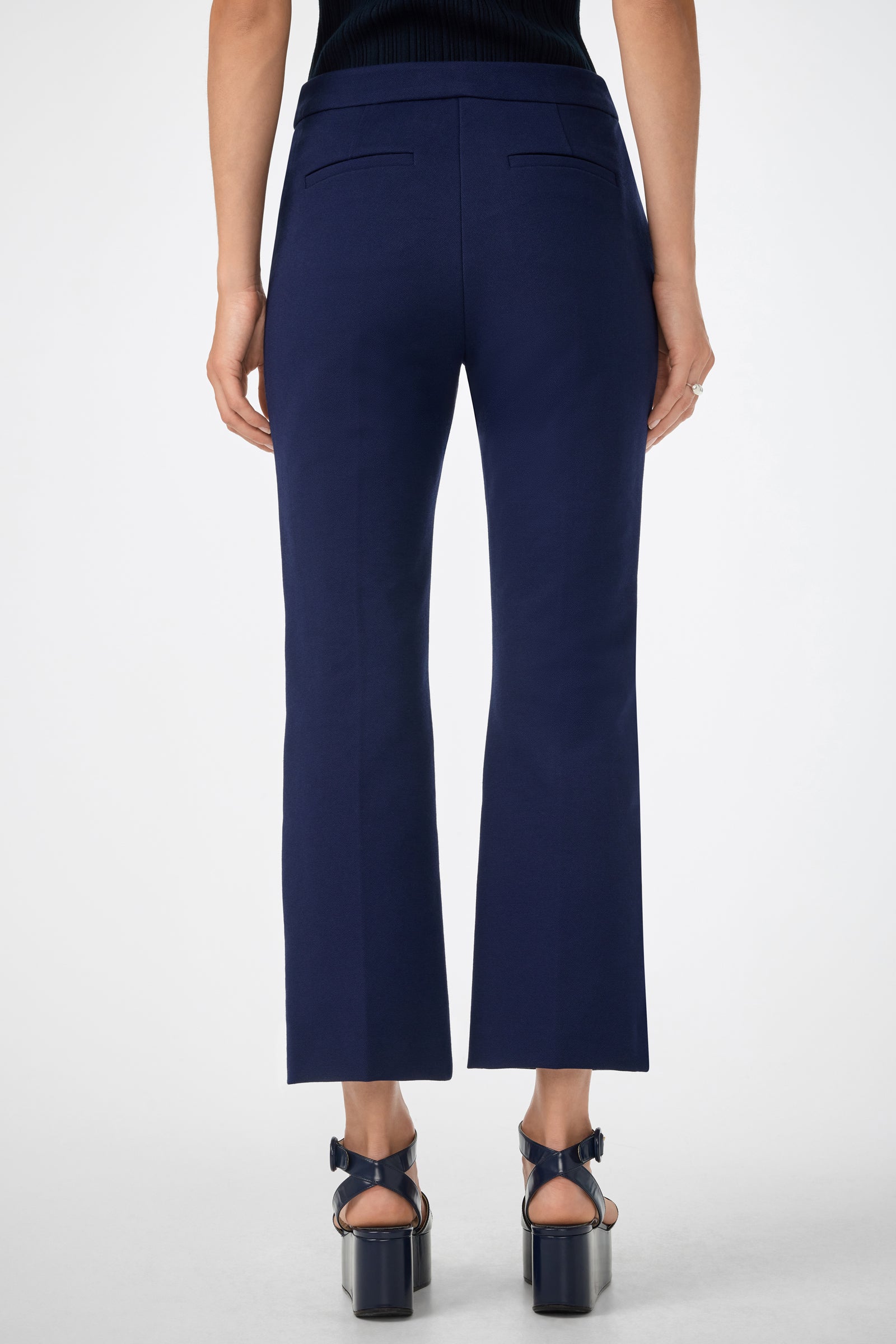A person shown from the back against a plain white background wears the Banshee Pant in navy blue, featuring a cropped, straight-leg design, paired with black high-heeled sandals.