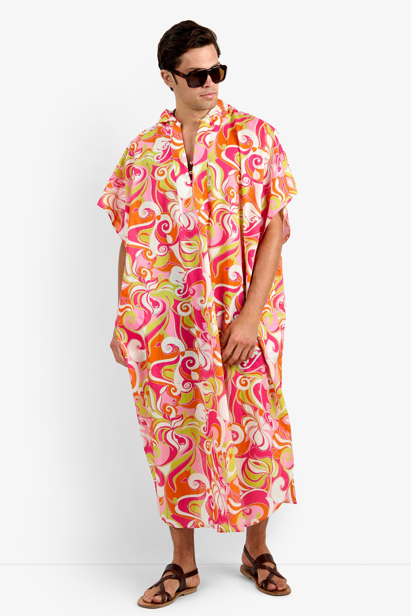 Wearing sunglasses and sandals, a person models the HURLEY CAFTAN in MULTI—a colorful, loose-fitting, hooded style crafted from soft 100% cotton with a vibrant swirl pattern—standing against a plain background.
