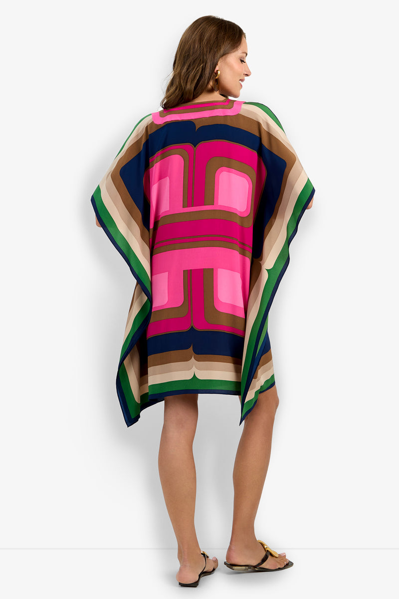 Woman standing with her back to the camera, wearing Vintage—a colorful, loose-fitting dress with bold geometric patterns in pink, blue, green, and beige—paired with flat sandals.