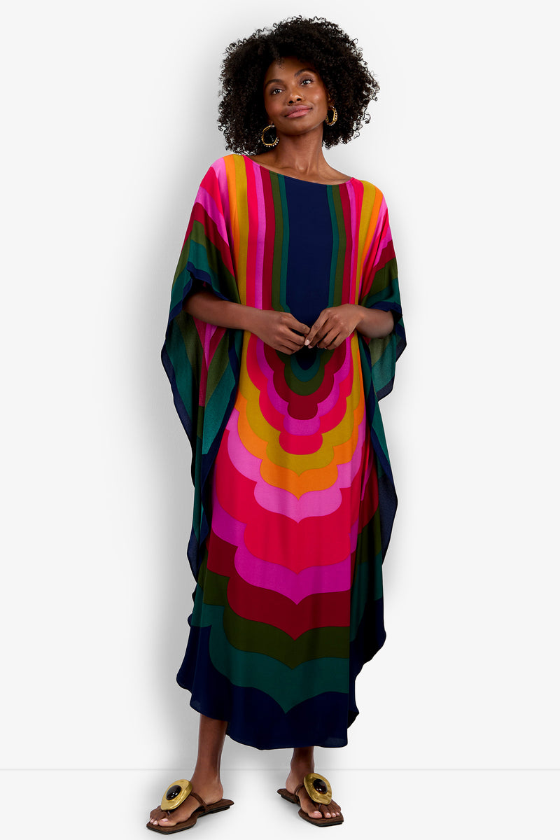 A woman wearing the Vintage Moroccan Geo Caftan, a long and loose dress with bold, colorful concentric patterns, stands smiling with her hands at her sides.
