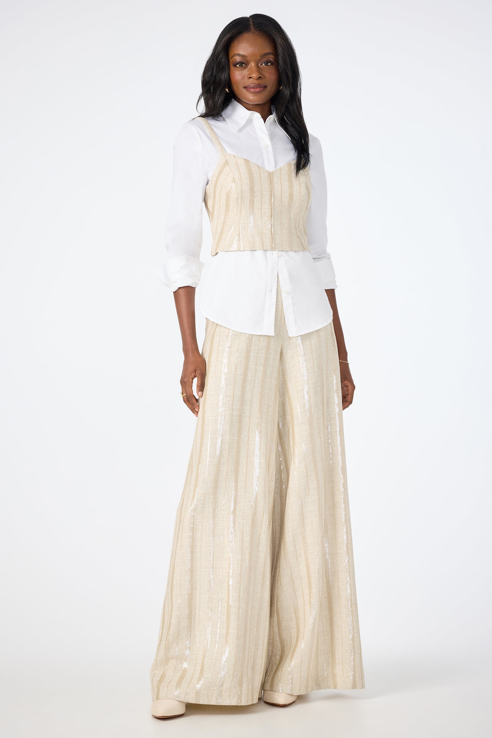 A woman stands against a plain background, wearing Nice Wide-Leg Pants with a cream sleeveless top over a white button-up shirt and cream shoes. She faces forward with a relaxed expression.