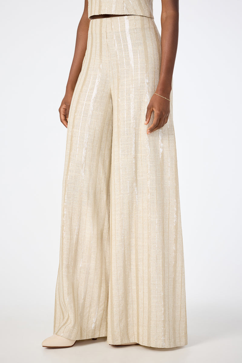 Model wears Nice Wide-Leg Pants—high-waisted, wide-leg, cream with subtle vertical stripes and a light-reflective texture—shown from shoulder to feet, styled with neutral pointed-toe shoes and a delicate bracelet.