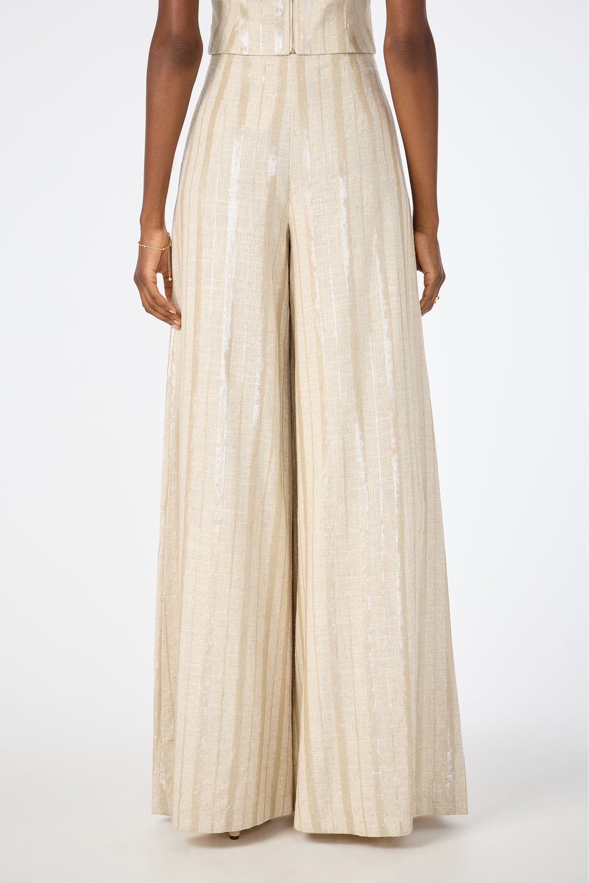 A person is shown from the back wearing Nice Wide-Leg Pants in high-waisted, light beige fabric with subtle vertical shimmery stripes, standing against a plain white background.
