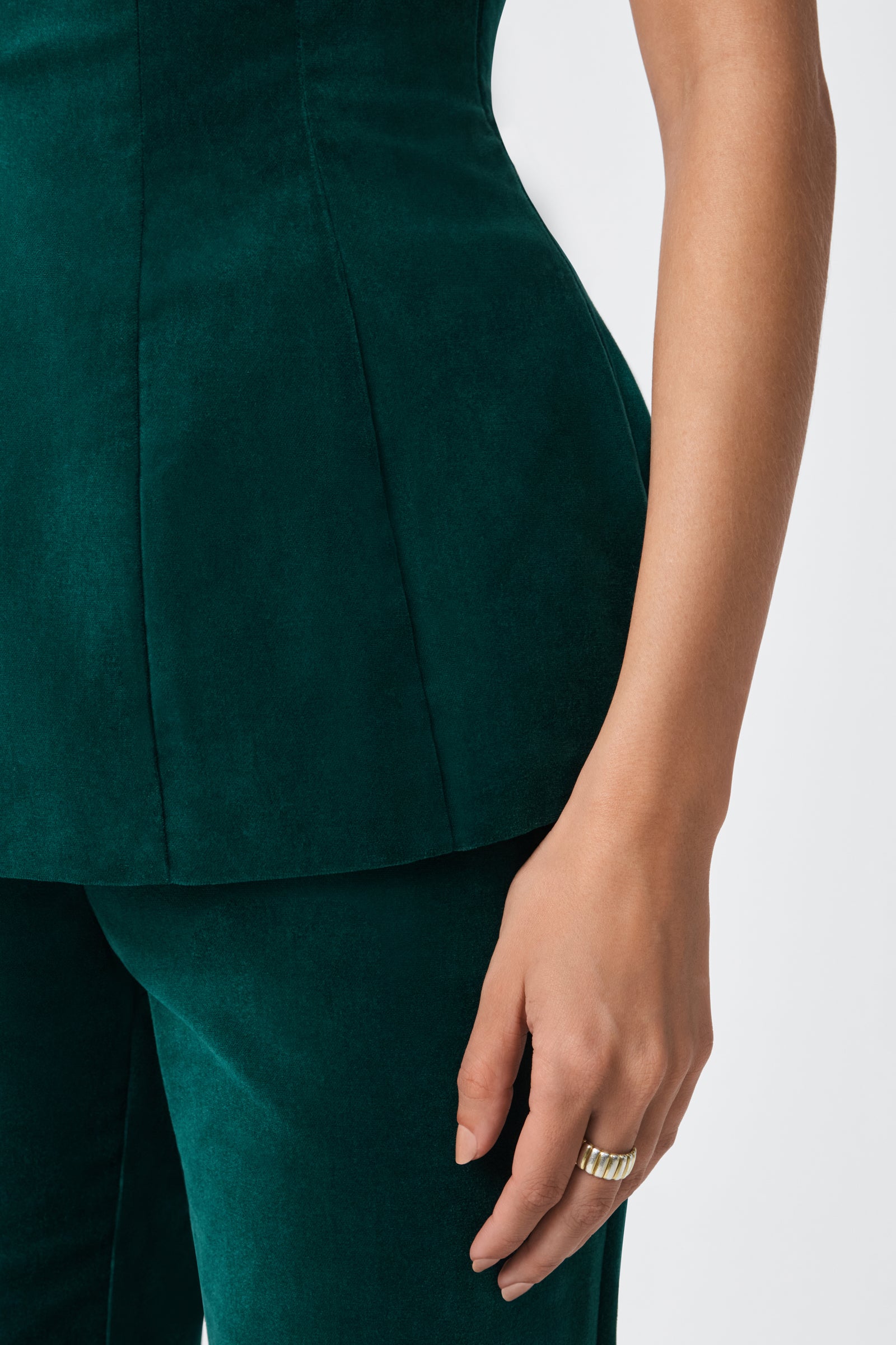 A person wears the Finale Top, a fitted dark green velvet piece with matching pants. Only their torso, waist, and right arm are visible. A gold ring is on their middle finger against a plain, light background.