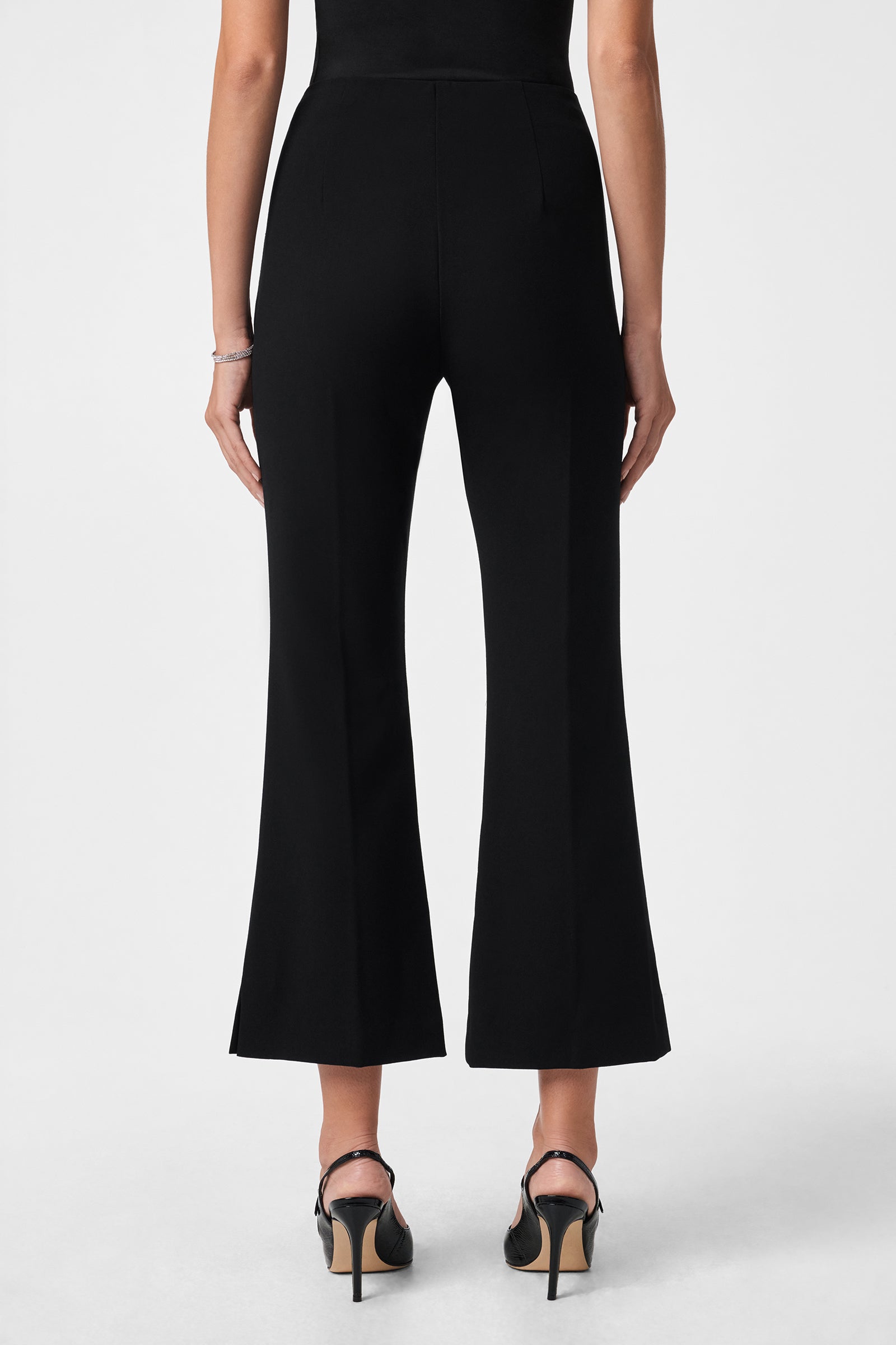 A person wearing the Luhrmann Pant in black, cropped and flared, paired with black heeled sandals, shown from the back against a plain white background.