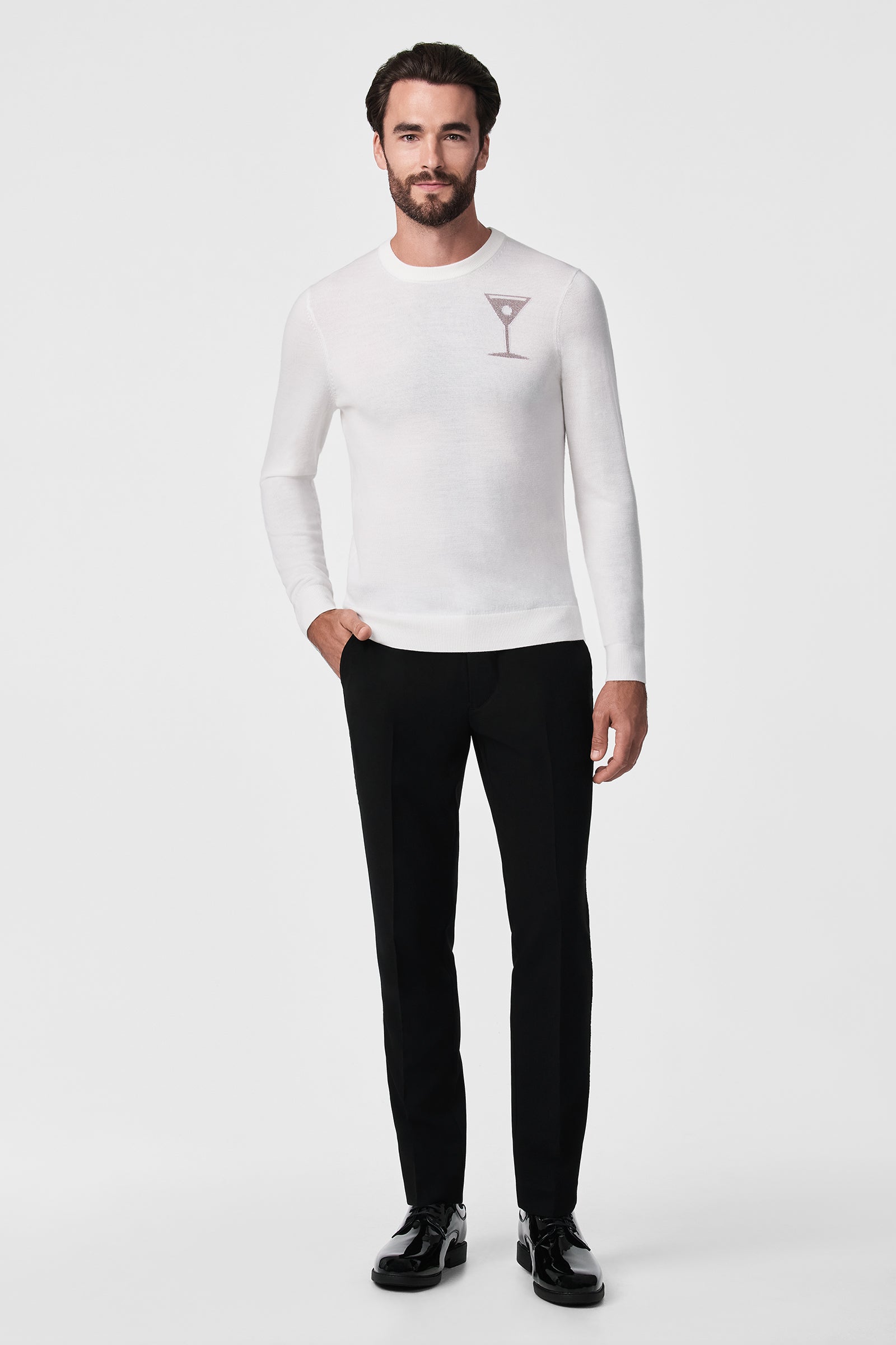 A man with dark hair and a beard wears the Martini Crewneck, a white long-sleeve shirt with a martini glass graphic on the chest, paired with black pants and black dress shoes, standing against a plain white background.