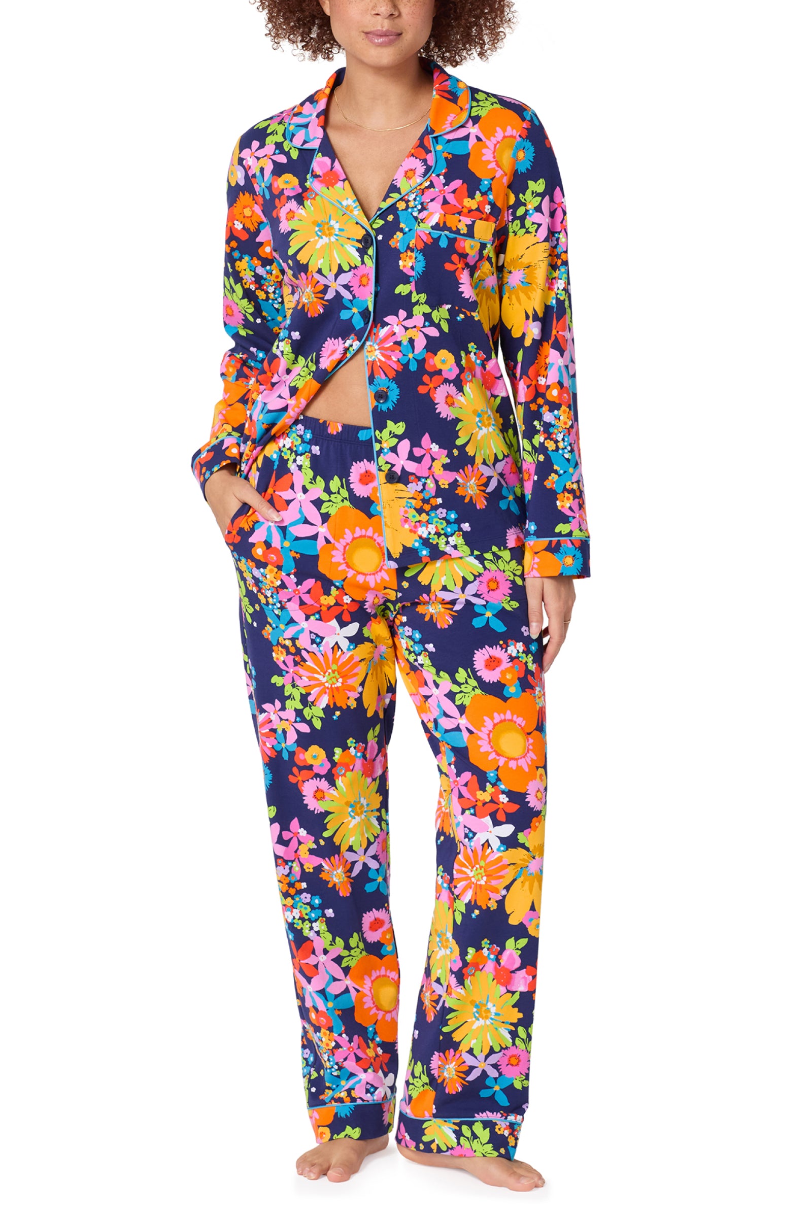 A person wearing the Classic PJ Set - Bay St Bloom, a colorful floral pajama set with long sleeves and pants on a dark blue background, stands barefoot against a white background.