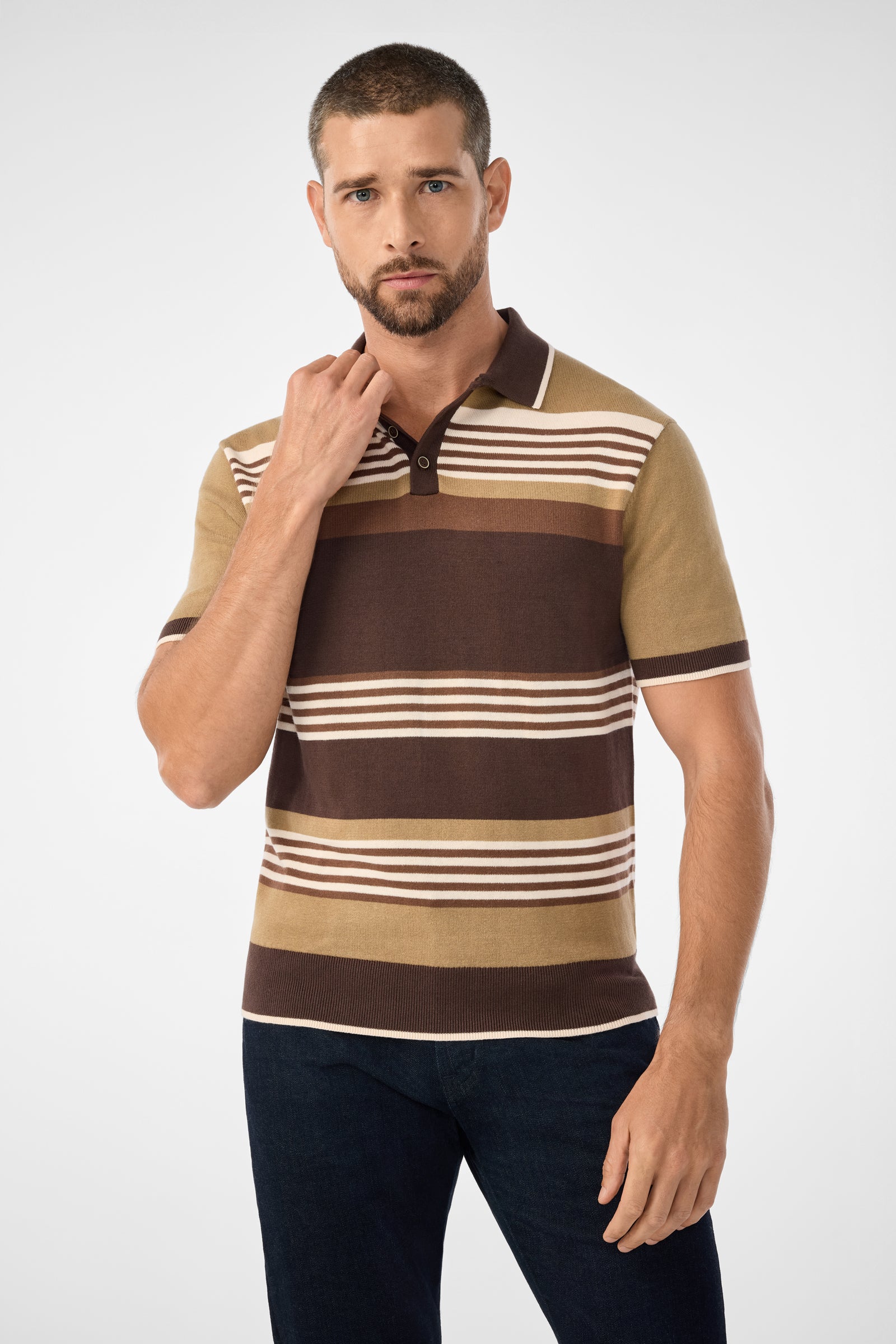 A man with short hair and a beard wears the walnut Edward Short-Sleeve Polo with dark jeans, standing against a light background. He looks at the camera neutrally, one hand near his collar.