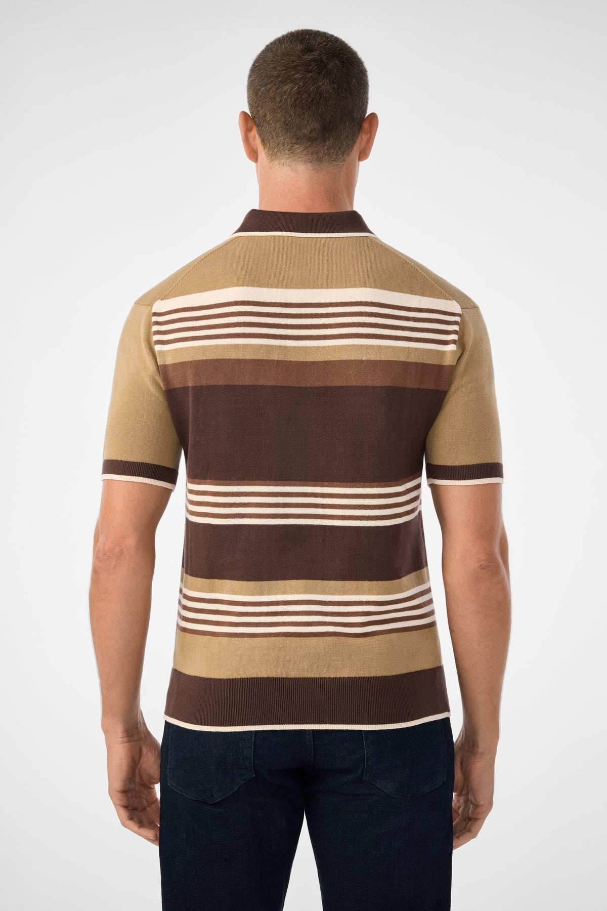 A man is seen from behind wearing the Edward Short-Sleeve Polo with horizontal brown, beige, and cream stripes, paired with dark jeans, against a plain light background.