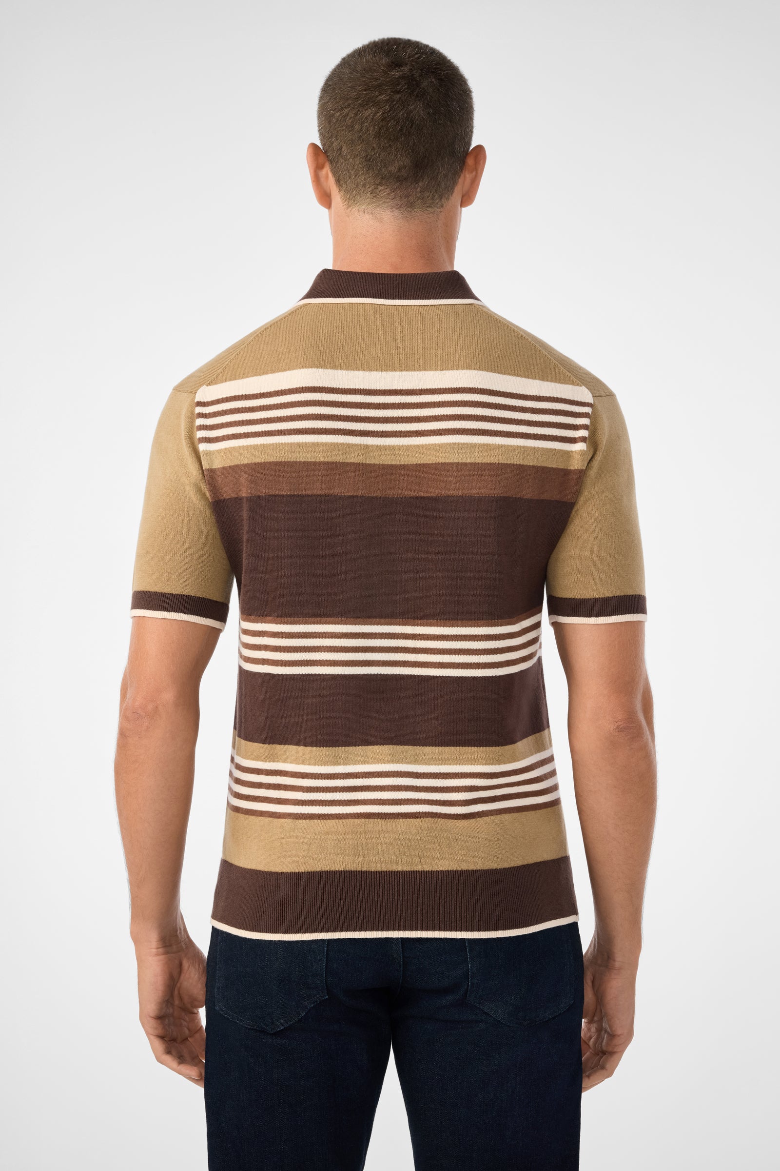 A man is seen from behind wearing the Edward Short-Sleeve Polo with horizontal brown, beige, and cream stripes, paired with dark jeans, against a plain light background.
