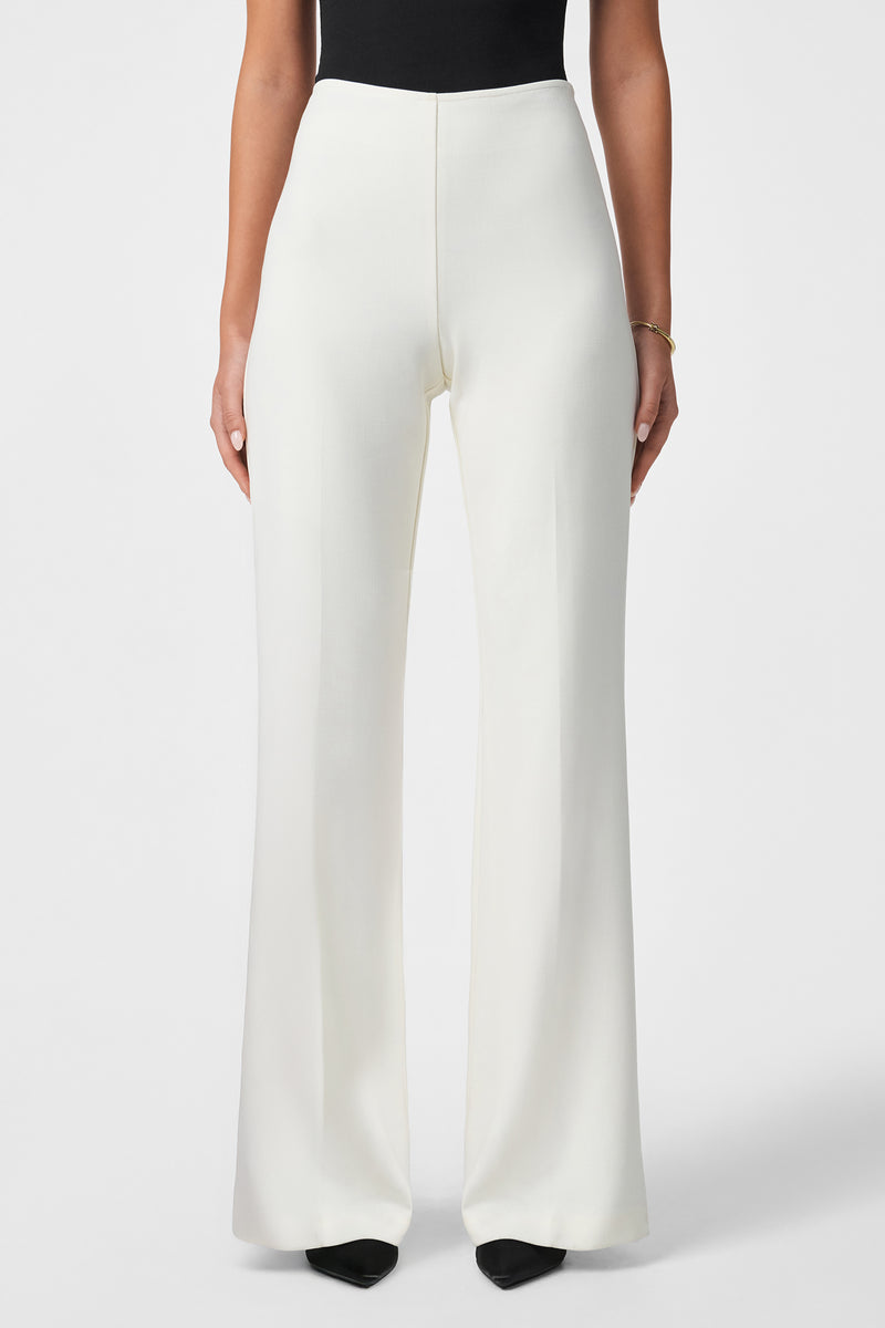 A person models the Chimayo 2 Pant—high-waisted, wide-leg white pants—with a black top and black pointed-toe shoes, standing against a plain white background. Only the lower half of the body is shown.