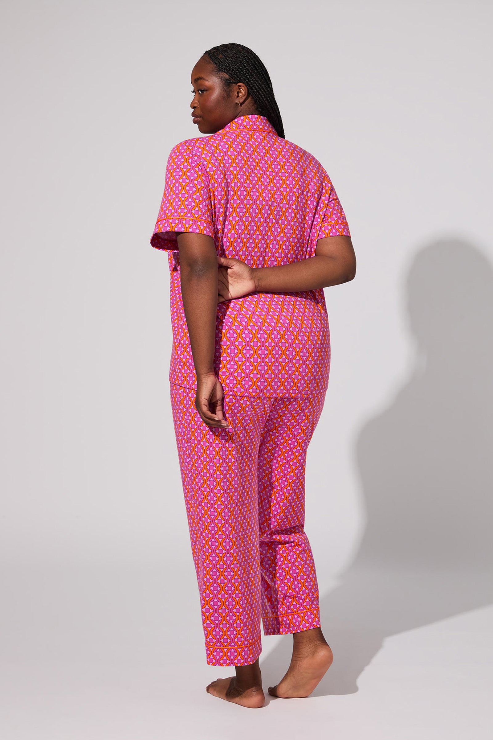 A person stands barefoot facing away, wearing the Crop Classic PJ Set - Chain Geo. One hand is behind their back and the background is plain and light-colored.