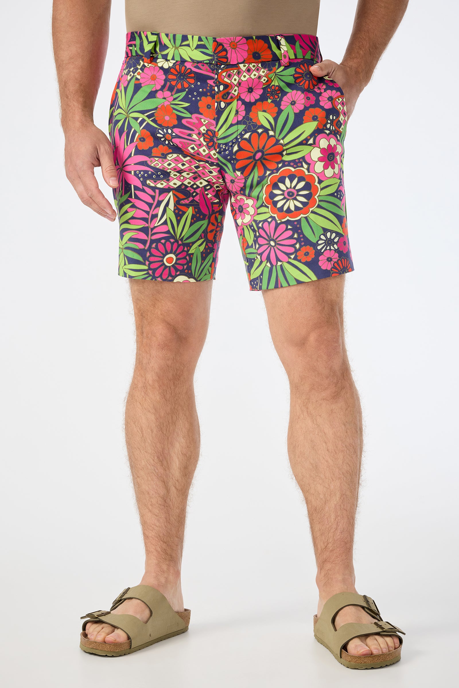 A person wearing the Lawrence Short in Fumi Floral and tan sandals stands against a white background. The shorts showcase a bold floral pattern with pink, green, red, and purple flowers plus green leaves.