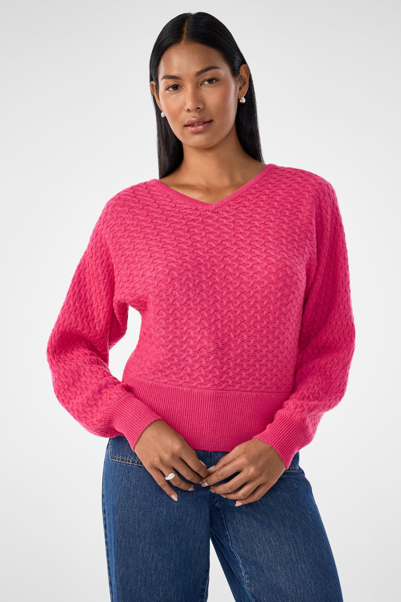 Woman with long dark hair wears the Lima V-Neck Pullover in Forrest Rose and blue jeans, standing against a plain light background and looking forward with a neutral expression.