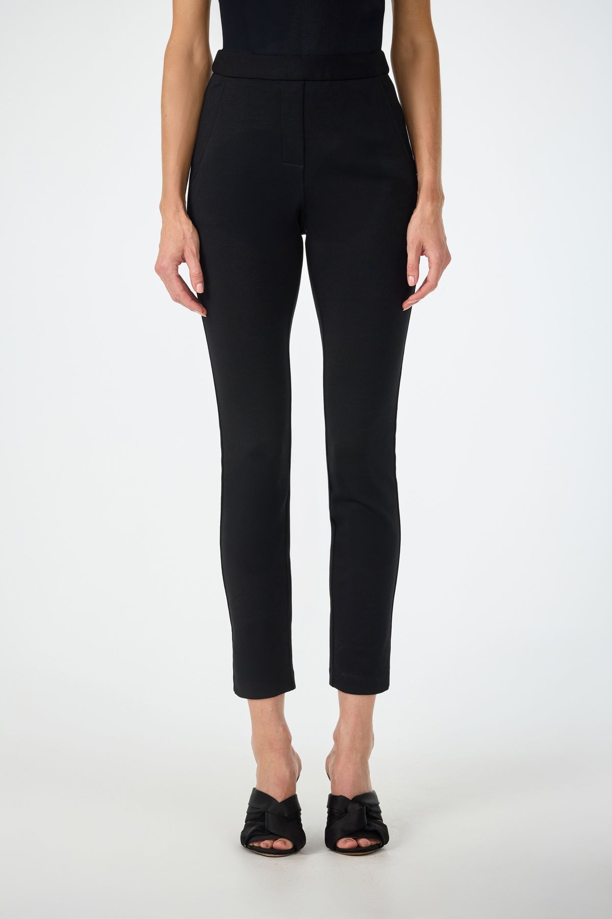 A person models the Honey Straight Leg Pants in black with black heeled sandals, standing against a plain white background. Only the lower torso and legs are visible.
